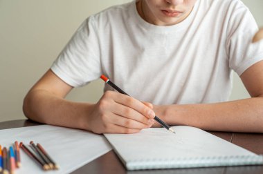 Genç bir çocuk resim çizer. Elinde kalem olan bir gencin eli. Yaratıcı hobi. Resim dersi. Yakın çekim ve seçici odaklanma.