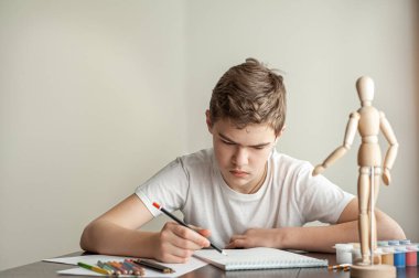 Genç bir beyaz çocuk resim yapmayı öğreniyor. Bir çocuk bir modelin üzerine bir adam çizer. Yaratıcı hobi. Çizim dersi.