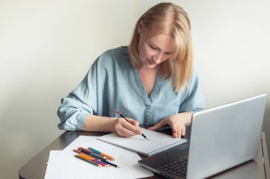 Hobiler ve online eğitim. Güzel sarışın bir kadın çevrimiçi bir derste albüm çiziyor. Bir kadın dizüstü bilgisayarın önünde kalemle resim çizer..