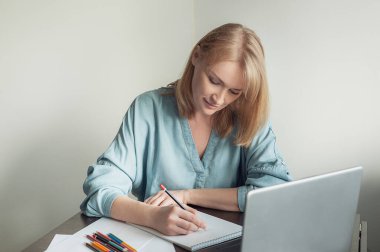 Hobiler ve online eğitim. Güzel sarışın bir kadın çevrimiçi bir derste albüm çiziyor. Bir kadın dizüstü bilgisayarın önünde kalemle resim çizer..