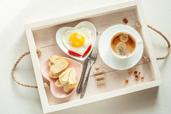 Día del Padre. Desayuno para papá. En la bandeja hay una taza de café y dos platos en forma de corazón con huevos revueltos y pan y mantequilla. Vista desde arriba. — Foto de Stock