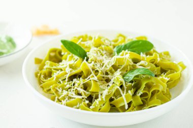 Beyaz bir masada beyaz tabakta ıspanaklı ve parmesanlı yeşil erişte. Temel malzemeler. Sağlıklı yemek.. 