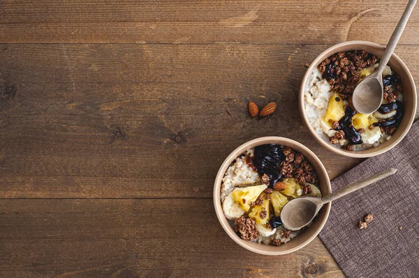 Harina de avena con piña, plátano y granola de chocolate en platos beige sobre una mesa de madera marrón. Un desayuno saludable. Un lugar para el texto. —  Fotos de Stock