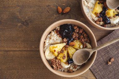 Kahverengi ahşap bir masada bej tabakta ananas, muz ve çikolata taneli yulaf ezmesi. Sağlıklı bir kahvaltı. Metin için bir yer.