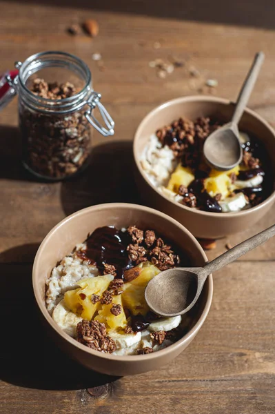 Zabpehely ananásszal, banánnal és csokoládé granolával bézs tányérokban barna fa asztalon. Egy kiadós, egészséges reggeli. Egy szöveges hely.. — Stock Fotó