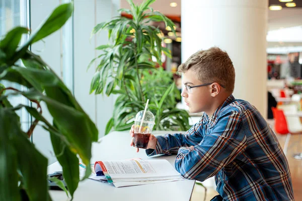 Um adolescente senta-se a uma mesa num café com um livro. Conceito de ensino à distância. Vida universitária. — Fotografia de Stock