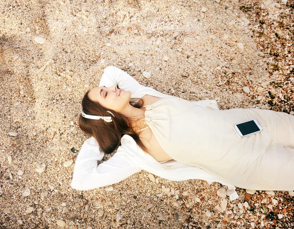 Glücklich lächelnde Frau, die auf einem Sand liegt und Musik hört — Stockfoto