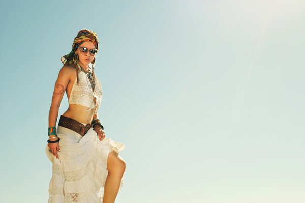 Young beautiful boho style woman standing outdoor against sky, vintage bleached colors