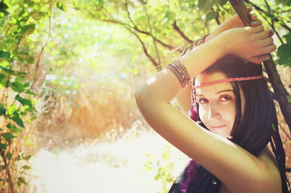 Jovem hippie menina com penas em seu cabelo e headband posando ao ar livre no parque ensolarado, olhando para a câmera e sorrindo — Fotografia de Stock