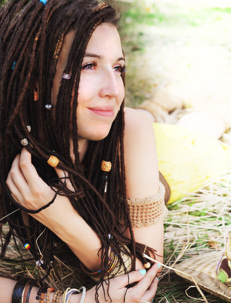 Спокойный улыбающийся портрет девушки с дредами, отдыхающей на сухой траве в парке
