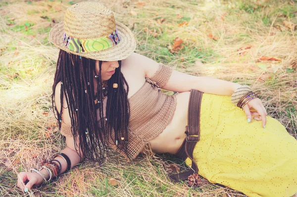 Retrato de mulher ao ar livre moda com dreadlocks, vestido em top de malha, saia amarela e chapéu de palha, descansando na grama seca no parque — Fotografia de Stock