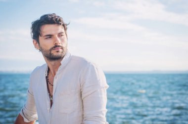 Büyük şehirde deniz kenarında boynunda el yapımı mücevherlerle gezen genç bir adam.