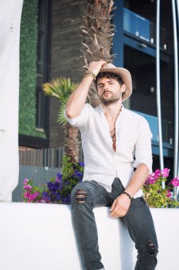 Şapka giymiş genç bir adam, şehir manzarasına karşı açık hava fotoğrafı.