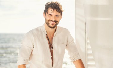 Beyaz gömlekli seksi adam portresi, kameraya bakıyor ve gülümsüyor.