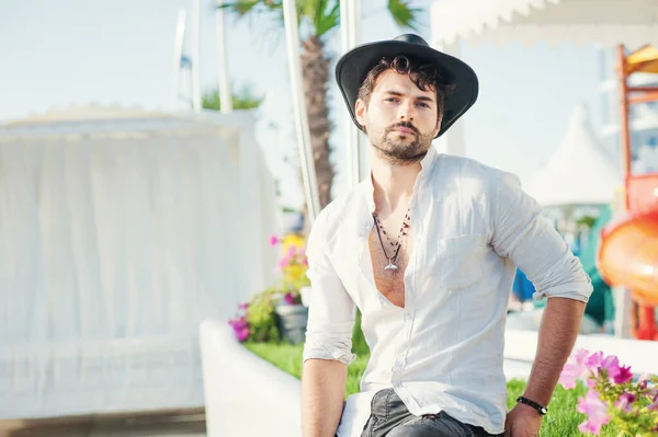 黒の帽子と白いシャツに身を包んだ深刻な男のモデル 観光熱帯都市の風景に対する屋外の写真 — ストック写真