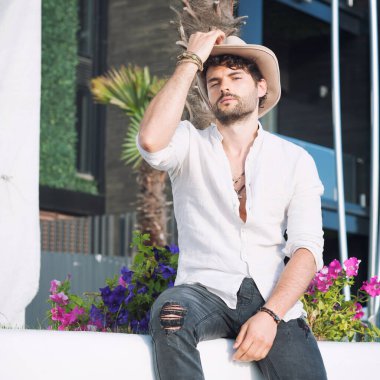 Young man dressed in hat, outdoor photo against city landscape