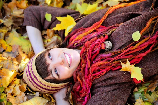 Gelukkig meisje in gebreide muts liggen in de herfst bladeren. — Stockfoto