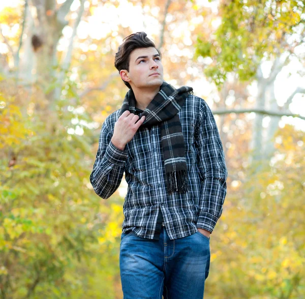 Man dressed in a plaid scarf walking in autumn park. — Stock Photo, Image