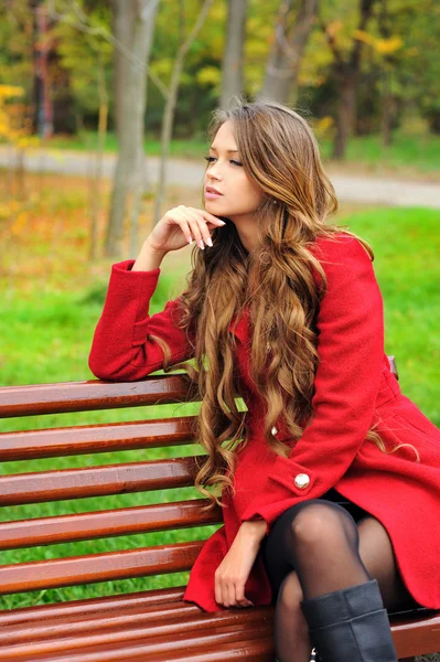 Mulher vestida de casaco vermelho sentado no parque de outono . — Fotografia de Stock