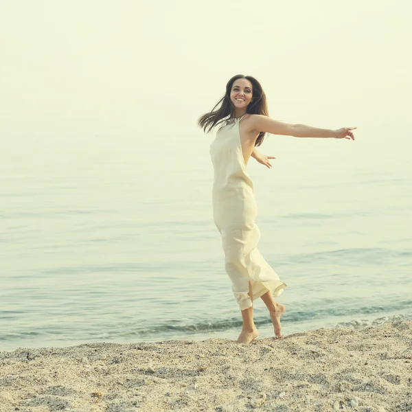 Mujer vistiendo vestido blanco largo divirtiéndose en una costa . — Foto de Stock