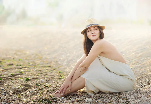 Hermosa mujer relajante sentada en una playa de arena de mar vestida con vestido blanco . — Foto de Stock
