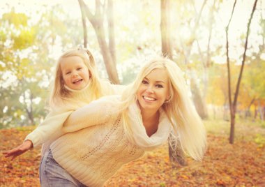 Happy cheerful mother holding smiling baby girl and play  together in sunny autumn park.