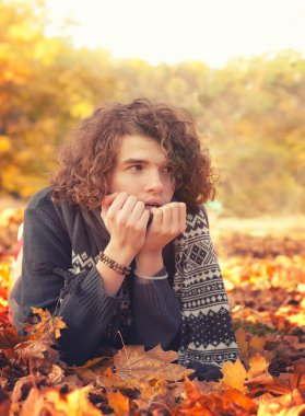 Man in knit sweater and scarf lying on autumn leaves, oudoor in autumn park.