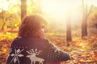 Man dressed in knit sweater with deers sitting  on autumn leaves in park.