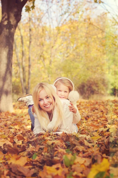 Smiling happy cute mother and little daughter lying on yellow maple leaves. — Stock fotografie