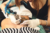 Hlavní tattooer ukazující proces tvorby tetování na břiše ženy.