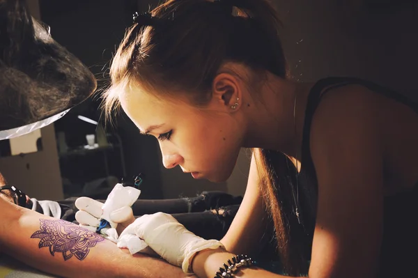 Портрет молодой милой женщины мастер татуировки делает татуировку на руке на пурпурном синем подобии будущей татуировки — стоковое фото