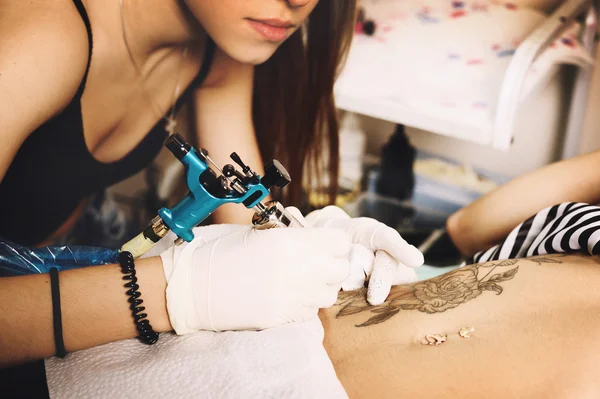Ung kvinna tattooer visar processen att göra en tatuering, svarta rosor design. — Stockfoto