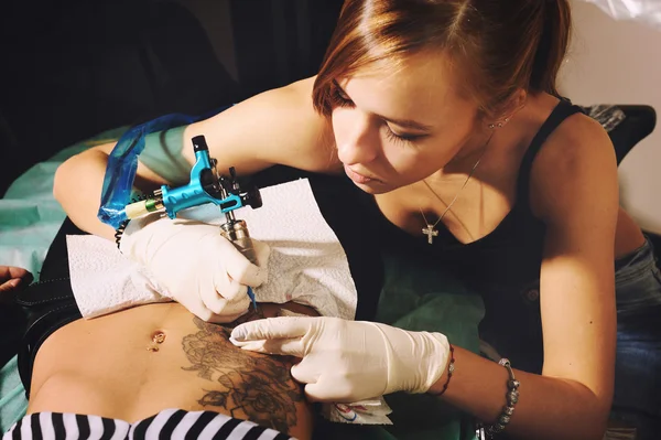 Young woman master correct black and white floral tattoo on a stomach. — Stock Photo, Image