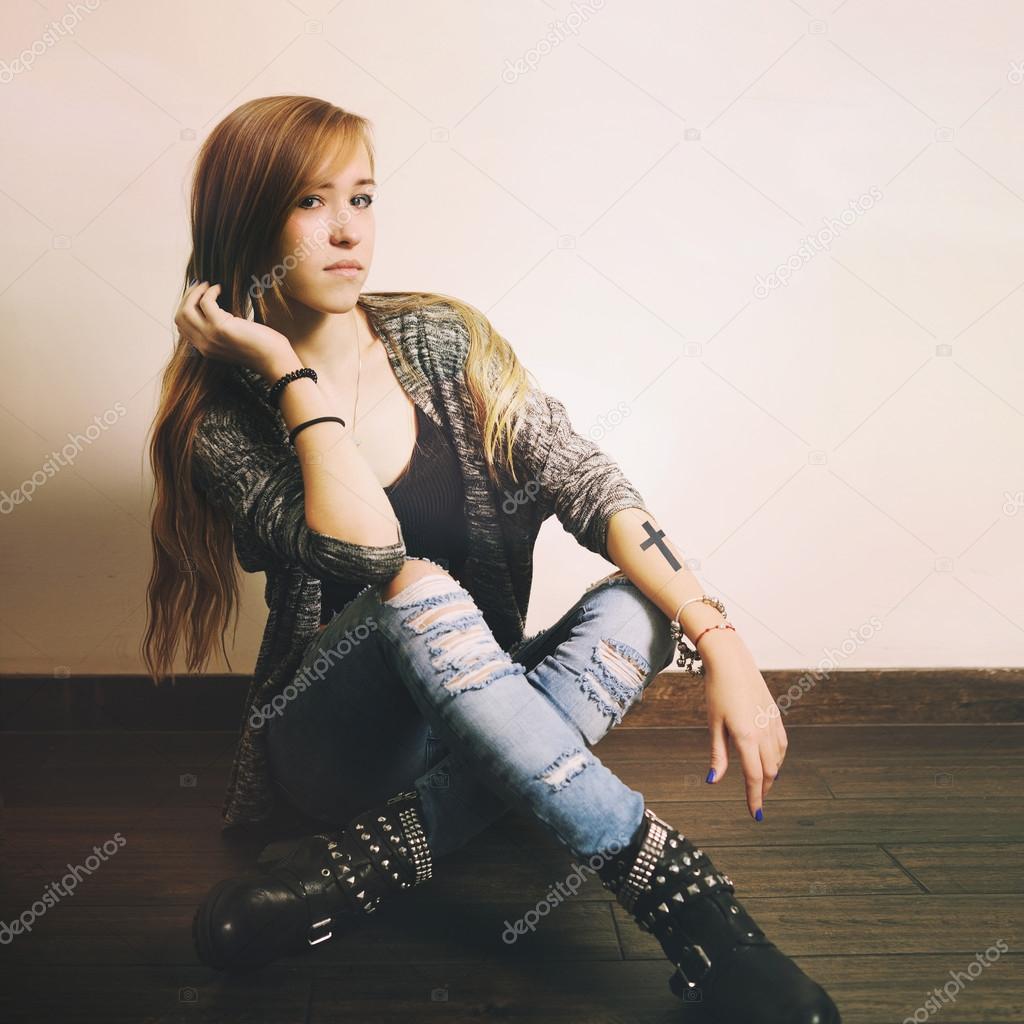 Young caucasian woman with cross tattoo on a hand sitting on a floor.