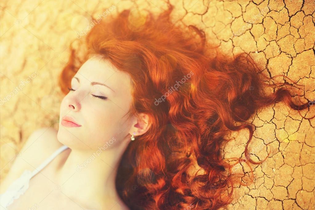 Sunny portrait of a relaxing young woman with chic long curly red hair lying on the cracked ground. Stock Photo by ©slena 93547316 Sunny portrait of a relaxing young woman with chic long curly red hair lying on the cracked ground. Stock Photo by ©slena 93547316