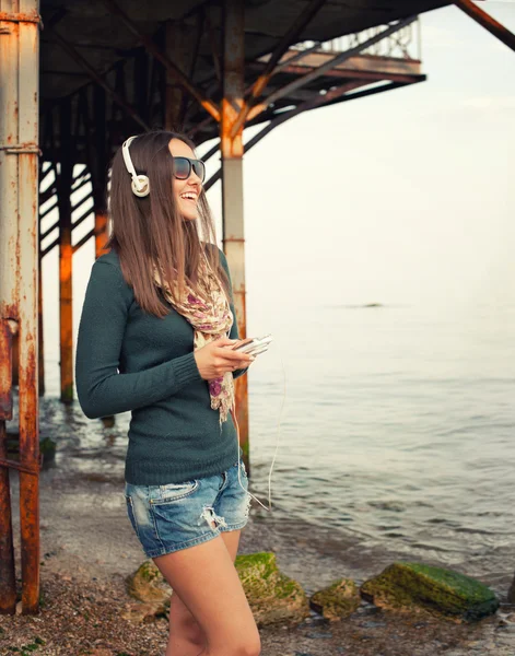 Felice donna sorridente godere di ascoltare musica con cameraphone contro il vecchio molo . — Foto Stock