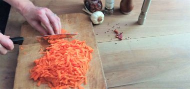 Masada havuç kesen kadın, yakın plan. Kesme tahtasında havuç kesen eller..