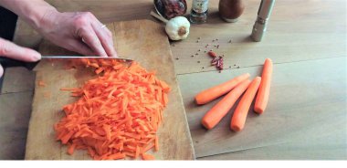 Masada havuç kesen kadın, yakın plan. Kesme tahtasında havuç kesen eller..