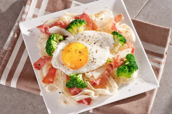 Tagliatelle pasta med broccoli, skinka och stekt ägg. — Stockfoto