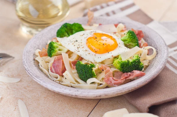Tagliatelle pasta with broccoli, prosciutto and fried egg. — Stock Photo, Image