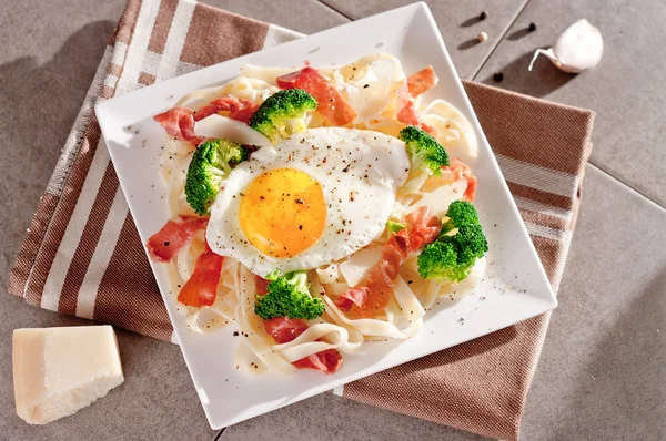 Tagliatelle tészta, brokkoli, sonka, tükörtojás. — Stock Fotó