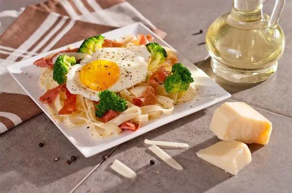 Tagliatelle pasta with broccoli, prosciutto and fried egg. — Stock Photo, Image