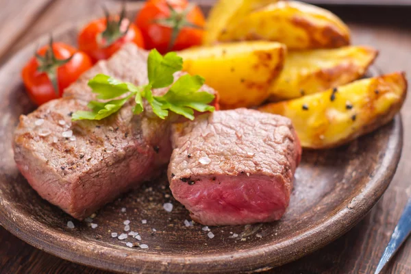 Rare beef steak on rustic plate witch baked potatoes and tomatoes — Stock Photo, Image