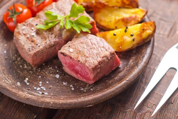 Rare beef steak on rustic plate witch baked potatoes and tomatoes — Stock Photo, Image