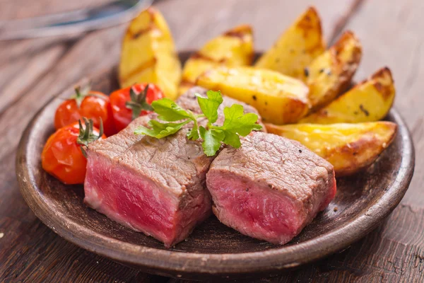 Rare beef steak on rustic plate witch baked potatoes and tomatoes — Stock Photo, Image