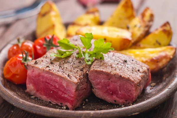 Rare beef steak on rustic plate witch baked potatoes and tomatoes — Stock Photo, Image