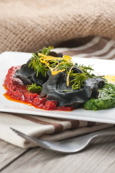 Black ravioli with spinach and garlic sauce tomato. — Stock Photo, Image