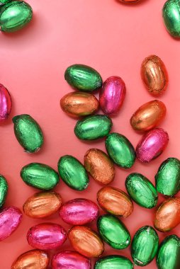 Büyük ve küçük renkli pembe, yeşil, turuncu ve altın folyo sarılı çikolatalı mini paskalya yumurtaları, şeftali turuncu arka planda. 