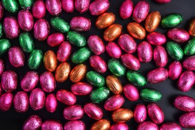 Pembe, yeşil, turuncu ve bronz folyo, siyah arka planda çikolatalı paskalya yumurtaları. 