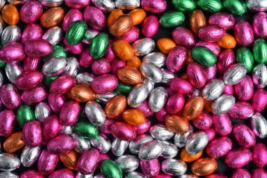 Pembe, yeşil, turuncu, gümüş ve bronz folyo, siyah arka planda çikolatalı paskalya yumurtaları.. 